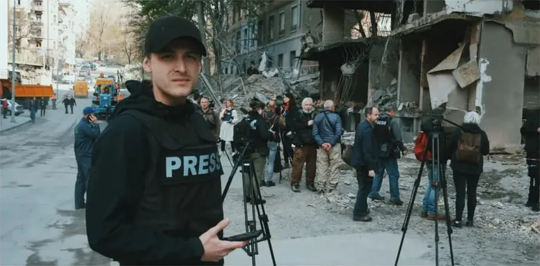 With a TV crew near damaged buildings